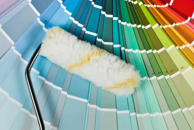 A paint roller resting on a fan of rainbow colour swatches