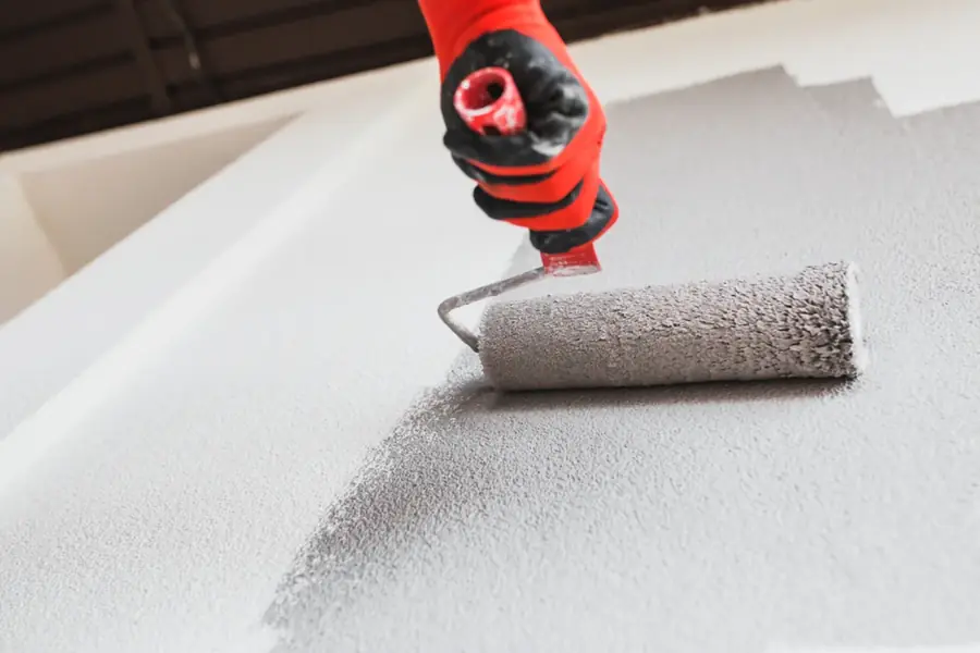 A gloved hand rolling grey paint onto a textured concrete surface