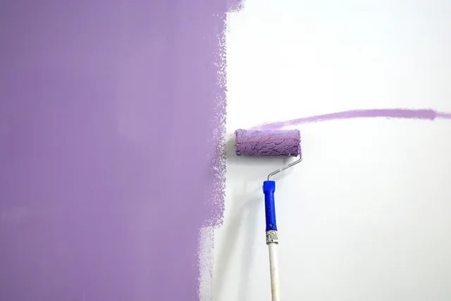 A roller applying purple paint to a wall mid-stroke in a newly built home